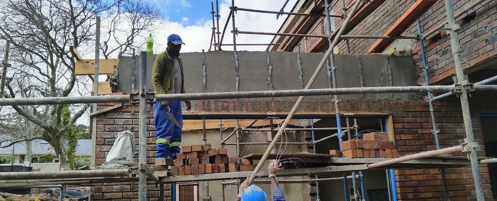 Bricklayer setting blocks on scaffolding above a brick wall
