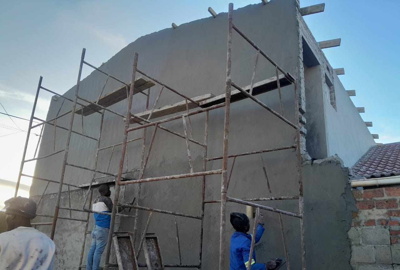 Plasterers finishing a tall gable wall from scaffolding