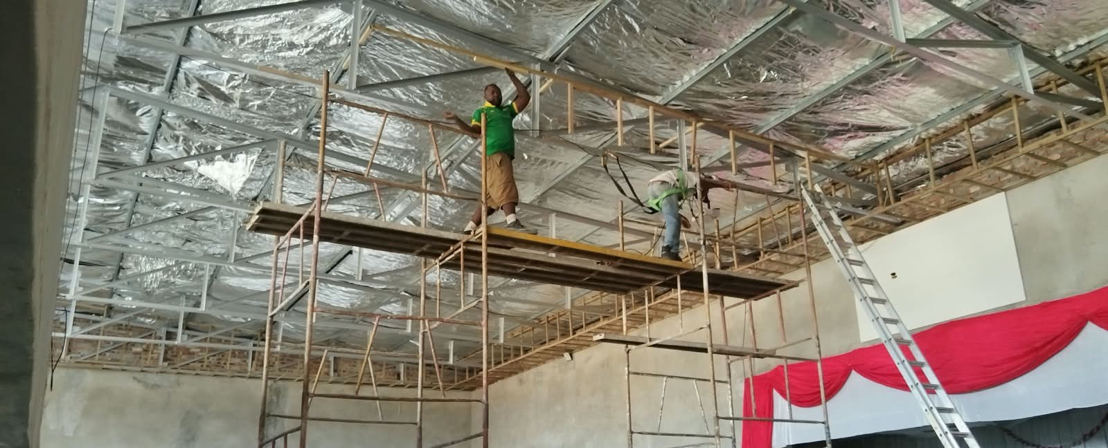 Team installing insulated ceiling framework from scaffolding inside a hall